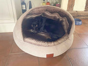 Small black dog curled up inside the Beige Deluxe Cocoon Dog Bed by Collared Creatures