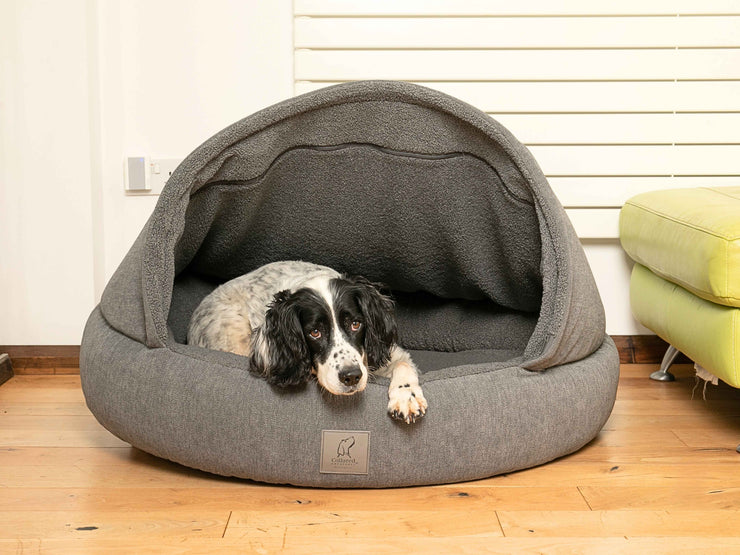 Black and white dog resting inside the grey cocoon bed with soft teddy fleece interior