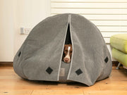 Brown dog peeking out from grey cocoon bed with curtains fully closed for privacy
