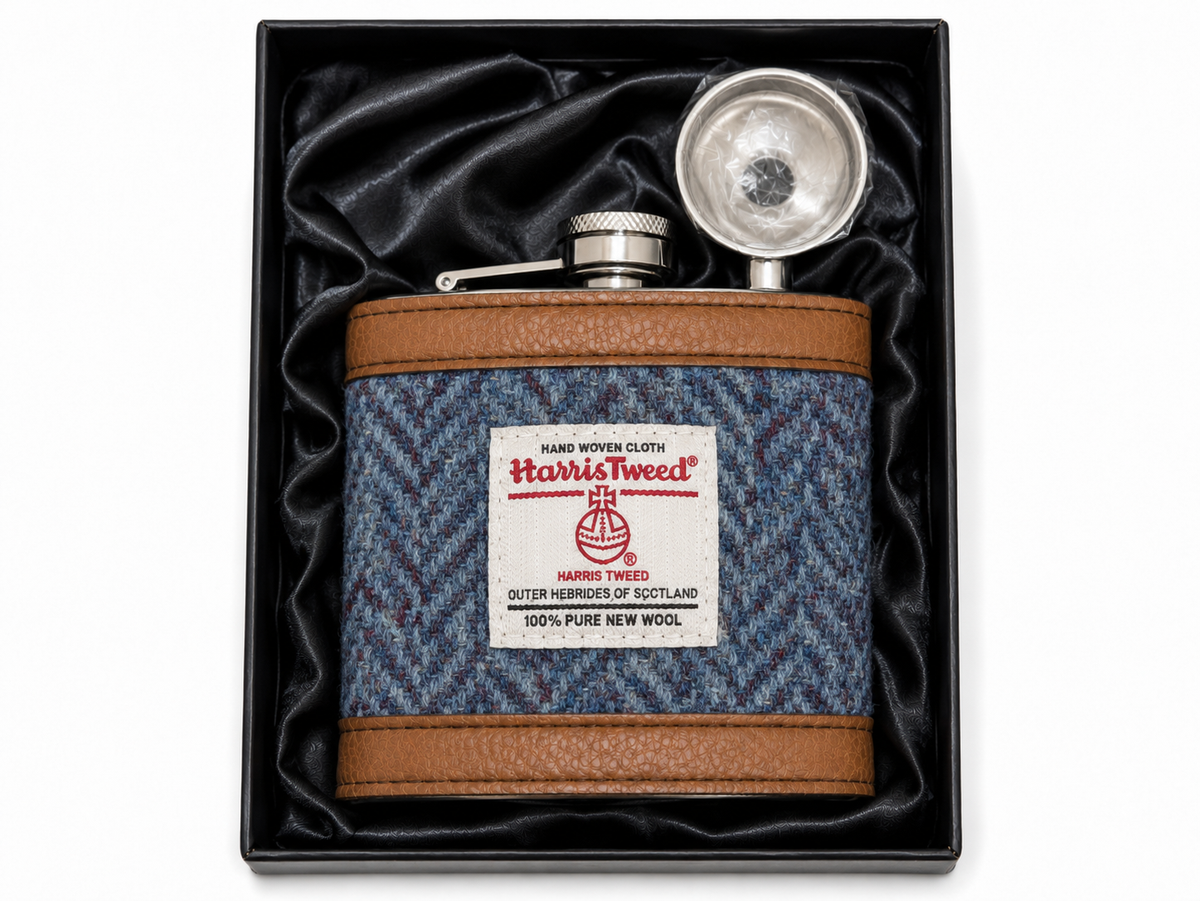 A Harris Tweed insulated flask presented in its black gift box with black satin lining. The flask features a blue and gray herringbone patterned body with brown faux-leather trim and a silver metal flask top.