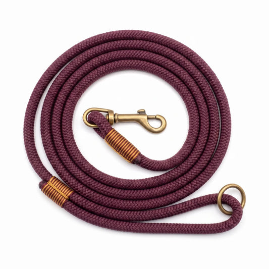 A coiled burgundy braided rope with brass-colored metal hardware, including a swivel snap hook, wrapped collars, and a ring, shown on a plain white background.
