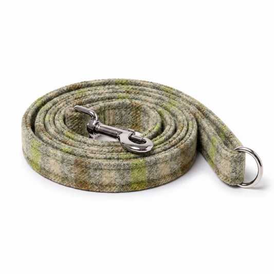 A coiled dog leash made of a textured plaid wool fabric in shades of olive green, beige, and brown, featuring a silver metal snap hook and a silver D-ring.