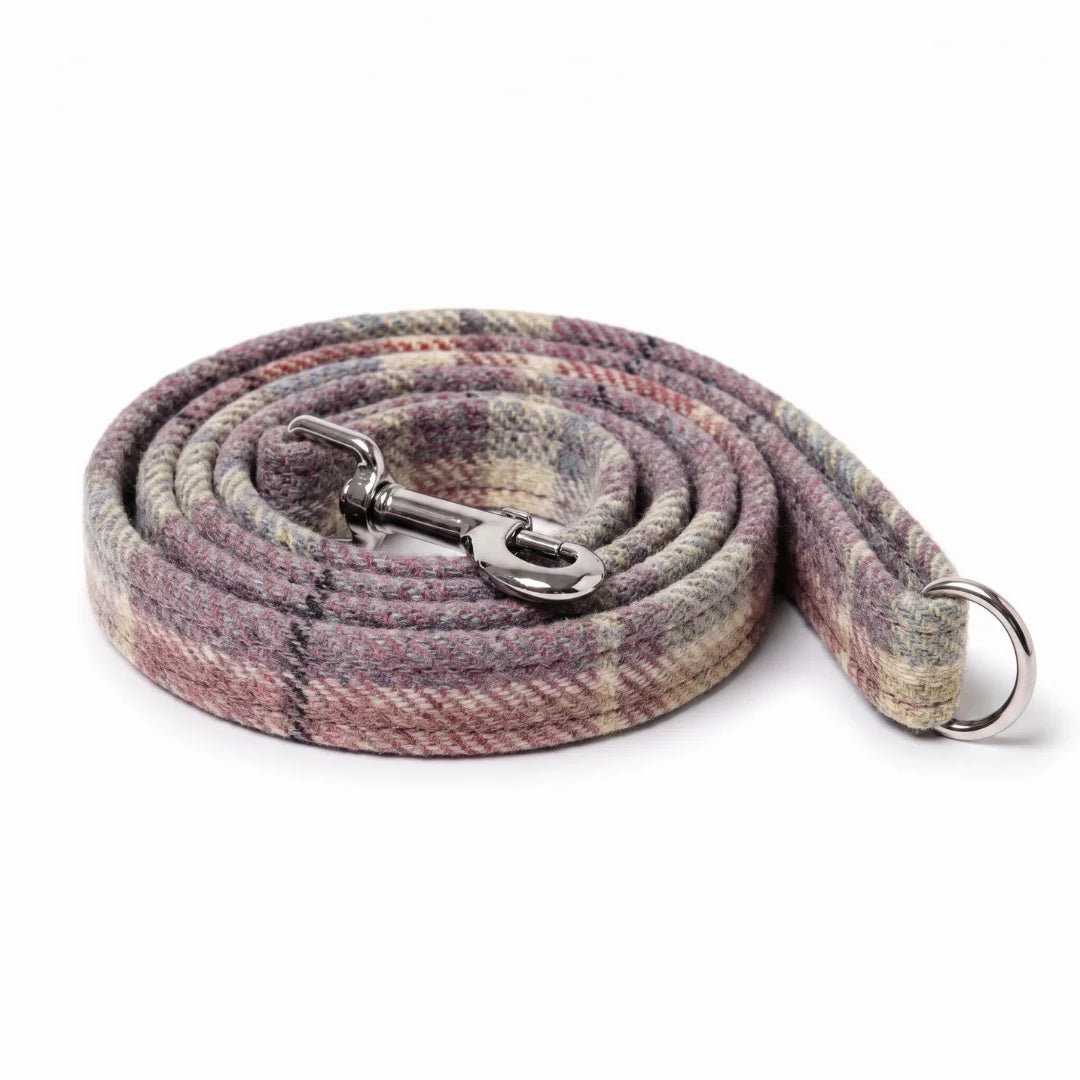 A coiled woven dog leash with a plaid pattern in muted pink, beige, and gray tones, featuring a silver metal snap hook and a silver D-ring, set against a plain white background.