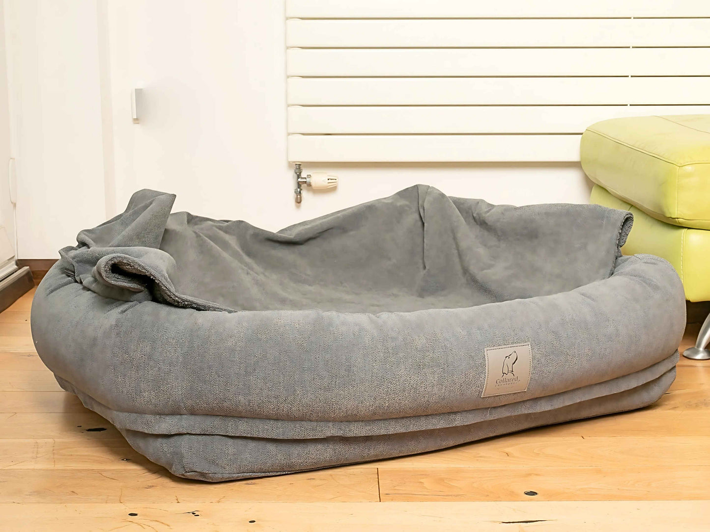 Grey bolster dog bed with hood laid down, creating an open nest-like sleeping area