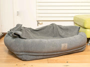 Grey bolster dog bed with hood laid down, creating an open nest-like sleeping area