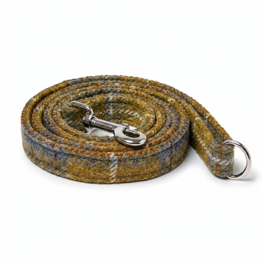 A coiled woven dog leash with a silver metal snap hook and ring, featuring a textured plaid pattern in mustard yellow, brown, and b on a white background.ue