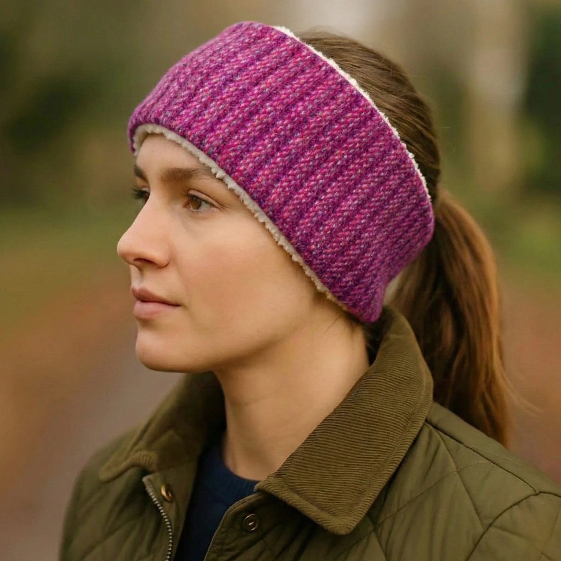 Person wearing a raspberry harris tweed knitted headband and green jacket outdoors