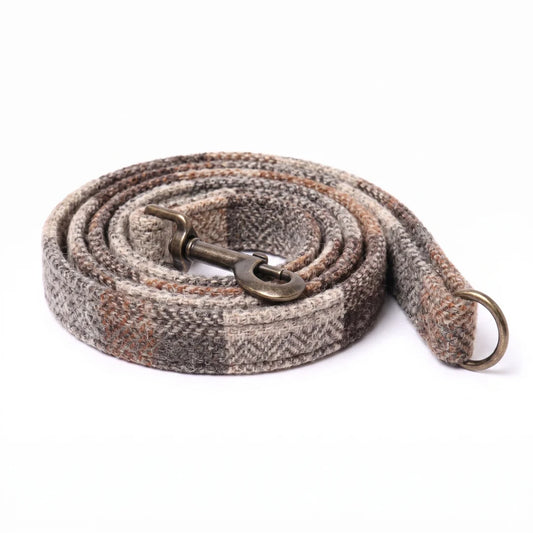 A woven horse lead rope with a herringbone pattern in gray, brown, and beige, featuring an antique bronze metal snap hook and a matching ring, coiled on a white background.