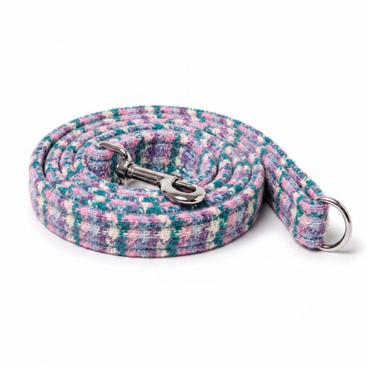 A woven dog leash with a multicolor pattern of pink, teal, purple, and white, featuring a silver metal snap hook and a silver D-ring, shown on a white background.