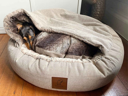 Dachshund tucked inside beige cocoon dog bed with plush faux fur lining