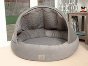Grey cocoon dog bed with structured hood placed by window