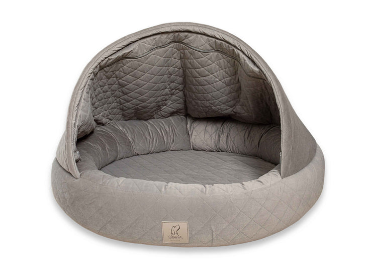 Grey quilted cocoon dog bed with open front and plush bolster