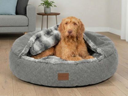 Dog sitting in a gray pet bed with a blanket in a living room.