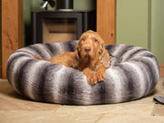 Large dog relaxing in a luxury grey striped faux fur donut dog bed by the fireplace
