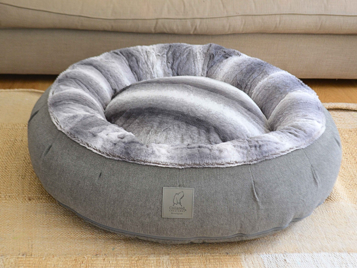 Grey donut dog bed with light and dark grey striped faux fur interior by Collared Creatures, placed on a woven rug in a cosy living room