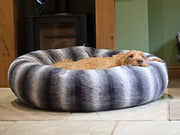Large dog resting in grey striped donut dog bed by the fireplace