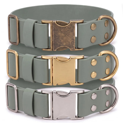 Three adjustable dog collars in a muted sage green color, stacked vertically. Each collar features a different metal finish on its hardware: an antique bronze buckle and ring on the top collar, a polished gold buckle and ring on the middle collar, and a silver buckle and ring on the bottom collar.