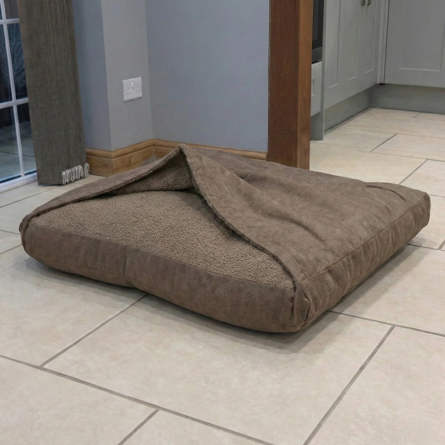 Brown covered pet bed on a tiled floor in a room with gray walls and wooden furniture.