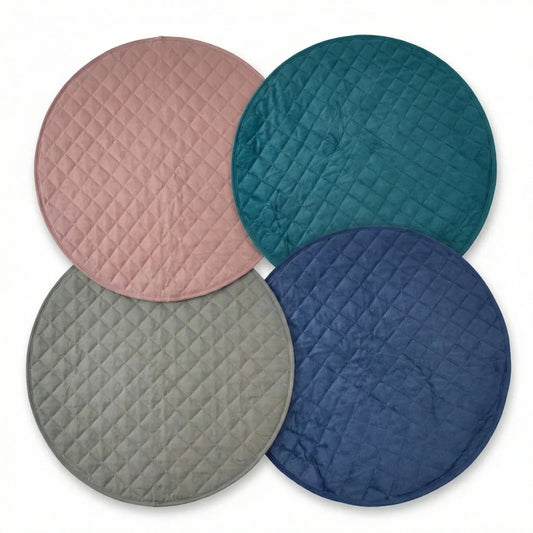 Four round quilted dog mats in pink, teal, gray, and blue on a white background.