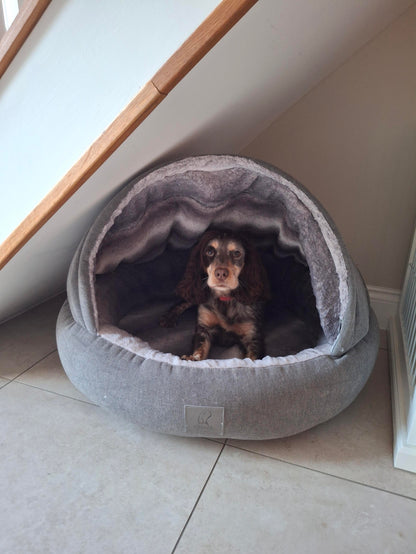 Dog inside a gray pet bed on a tiled floor.
