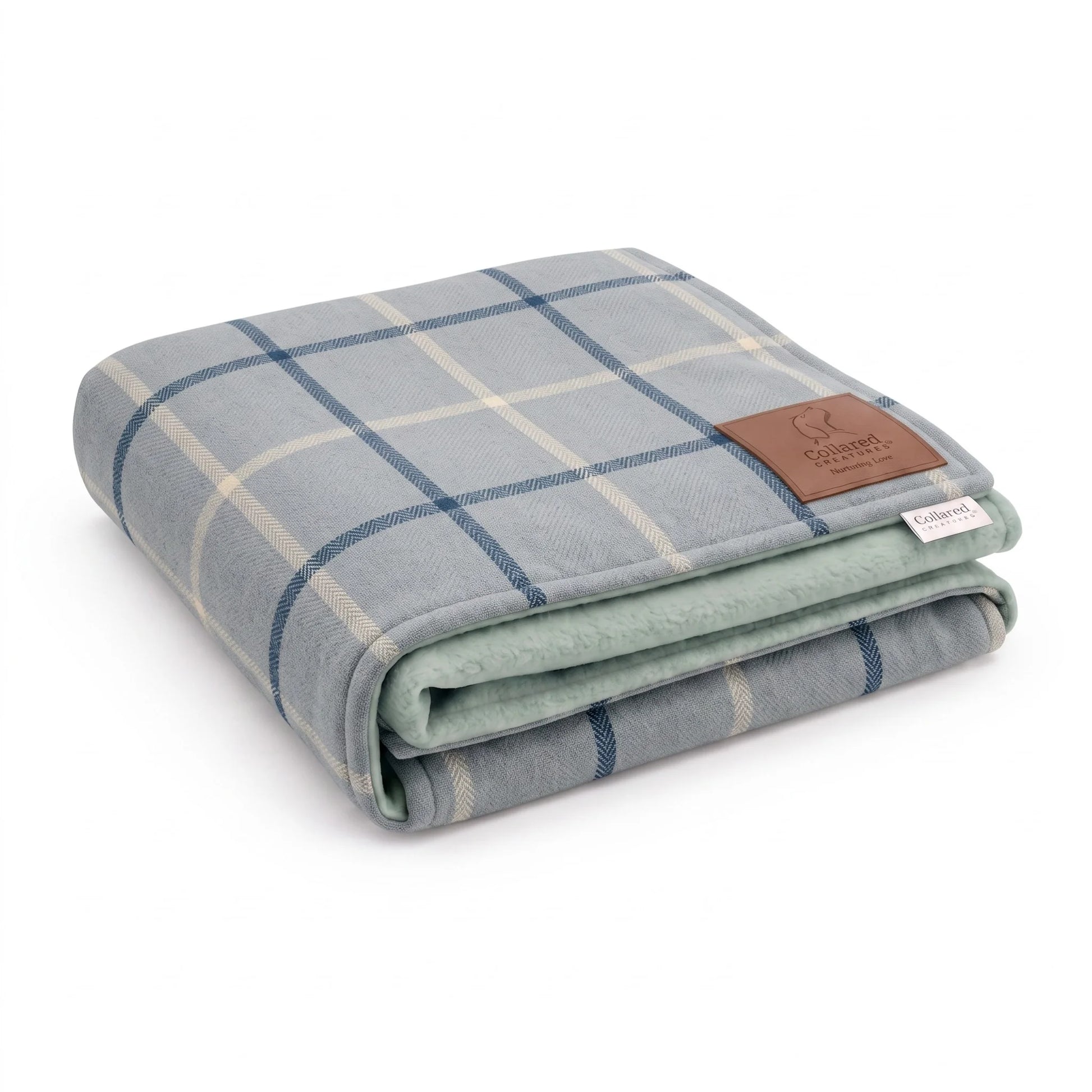 A folded plaid blanket in light gray and navy blue with a beige grid pattern, featuring a brown leather brand patch on the corner.