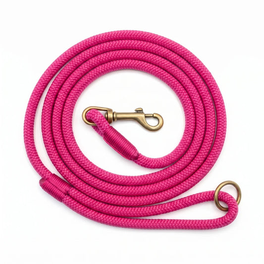A bright pink braided rope leash coiled on a white background, featuring a brass-colored metal clasp and a matching ring at the end.