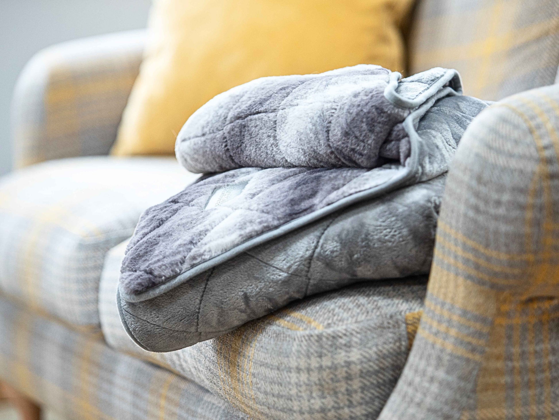 Quilted grey faux fur dog blanket draped over sofa with yellow plaid cushions