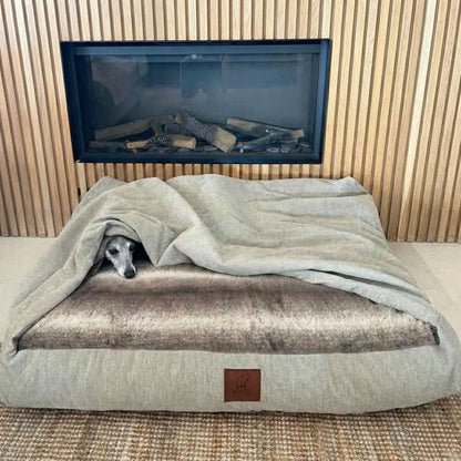 Dog lying on a large dog snuggle bed with a blanket, in front of a fireplace.