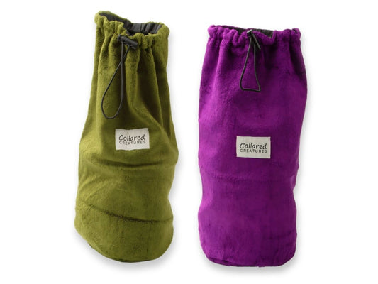 Two dog drying coat storage bags, one green and one purple, with a drawstring closure and a label showing the brand name 'Collared Creatures'.